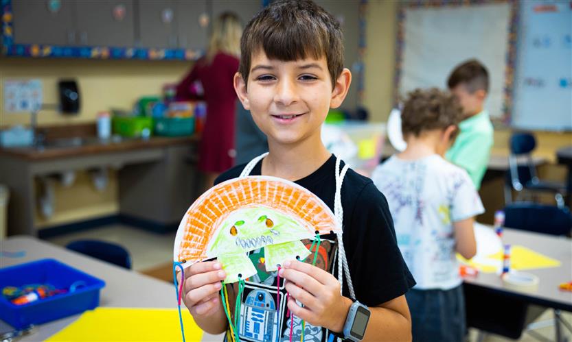 A boy wearing a black shirt smiles while holding a piece of art